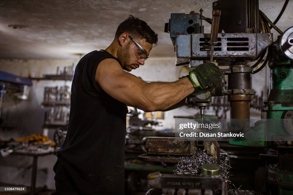 Steel worker, making few adjustment on a milling machine at the metal workshop