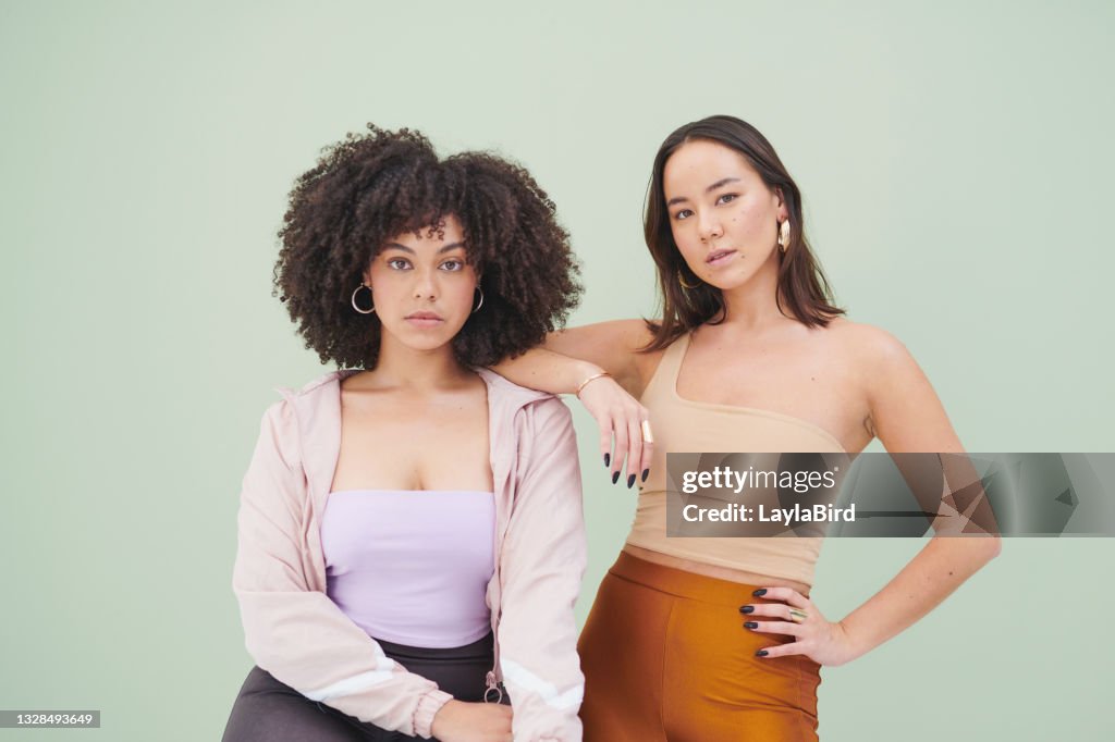 Studio portrait of two young woman posing against a green background