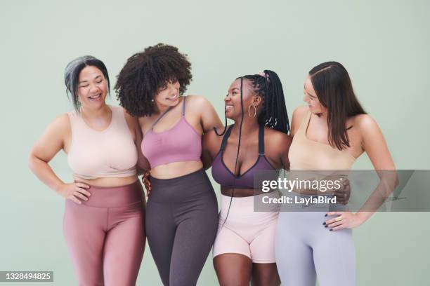 studio shot of a group of women embracing each other against a green background - plus size model fitness stock pictures, royalty-free photos & images