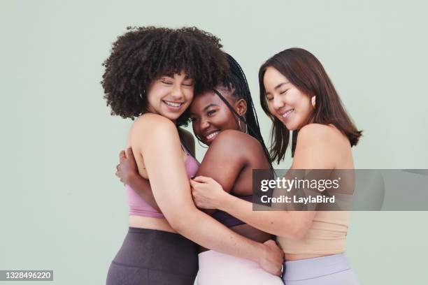 studio portrait of a group of young women embracing each other against a green background - friendship background stock pictures, royalty-free photos & images