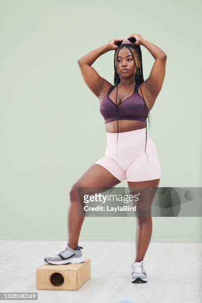full body studio portrait of a young woman lifting one leg on a wooden structure against a green background - female armpits imagens e fotografias de stock