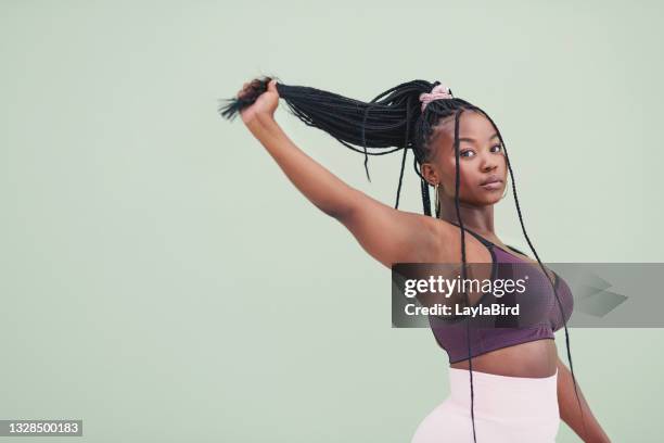 abgeschnittenes studioporträt einer jungen frau, die an den haaren zieht und vor grünem hintergrund posiert - pferdeschwanz stock-fotos und bilder