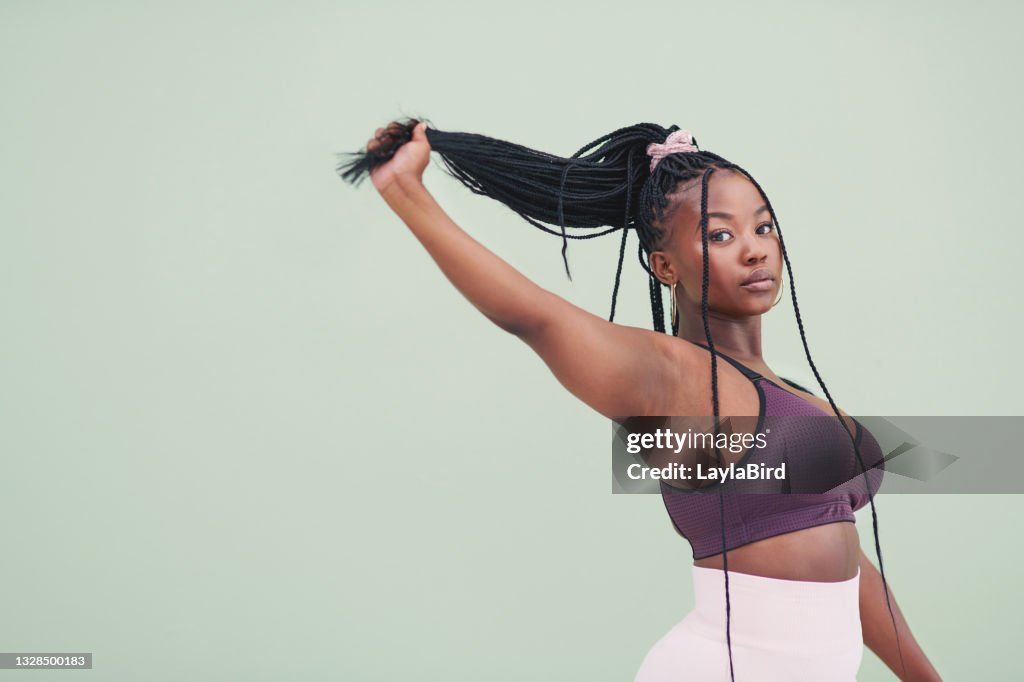 Cropped studio portrait of a young woman pulling her hair and posing against a green background