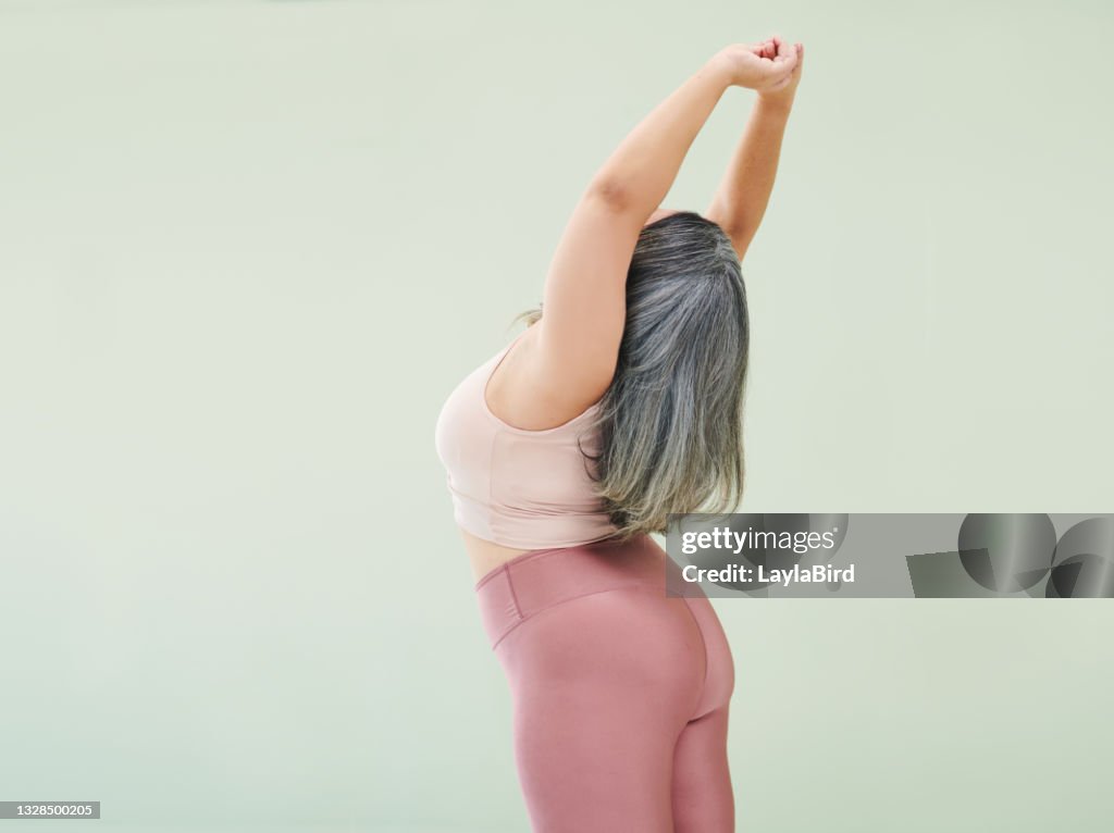 Rear studio shot of an unrecognizable woman stretching against a green background