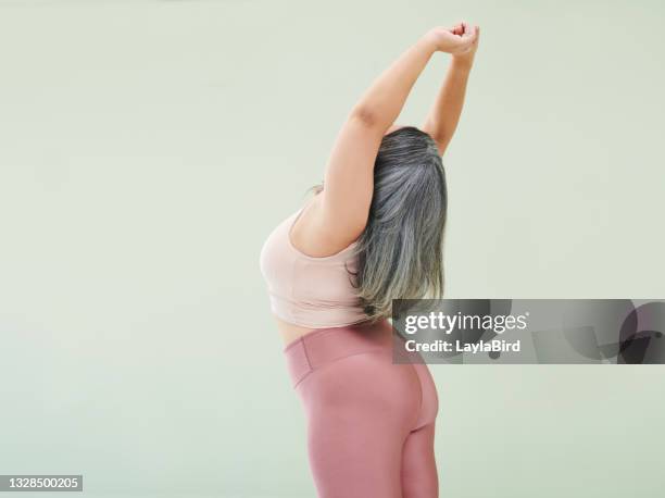 rear studio shot of an unrecognizable woman stretching against a green background - plus size fashion model stock pictures, royalty-free photos & images