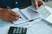 Man using calculate domestic bills on wooden desk in office and business working background.Young male checking balance and costs with U.S IRS 1040 form, Tax, statistics, and analytic research concepts.