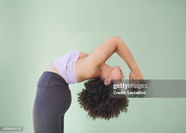 studio shot of a young woman bending over backwards against a green background - buigen lichaamsbeweging stockfoto's en -beelden
