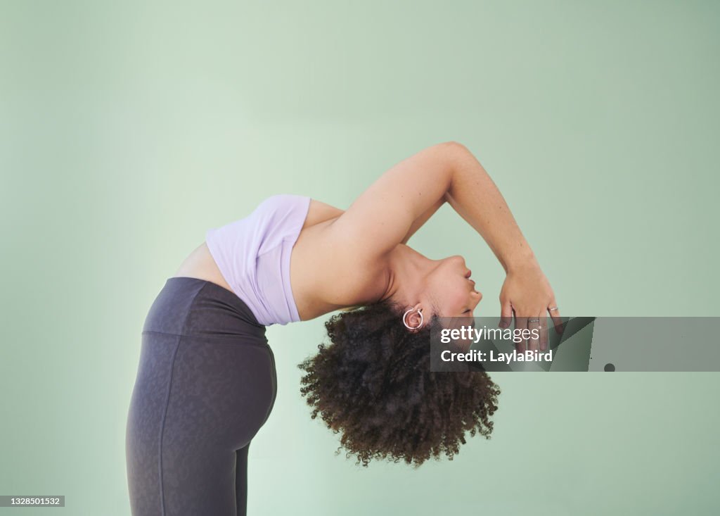 Studio shot of a young woman bending over backwards against a green background