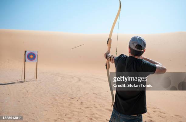 man practicing archery using bow and arrow to hit the target in the desert - rematar à baliza imagens e fotografias de stock