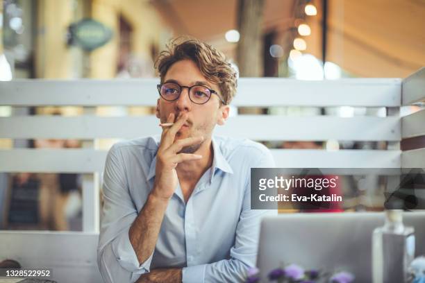 young man smoking a cigarette in a sidewalk cafe - tobacco workers stockfoto's en -beelden