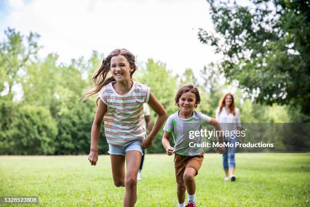 brother and sister running in the park - groene korte broek stockfoto's en -beelden