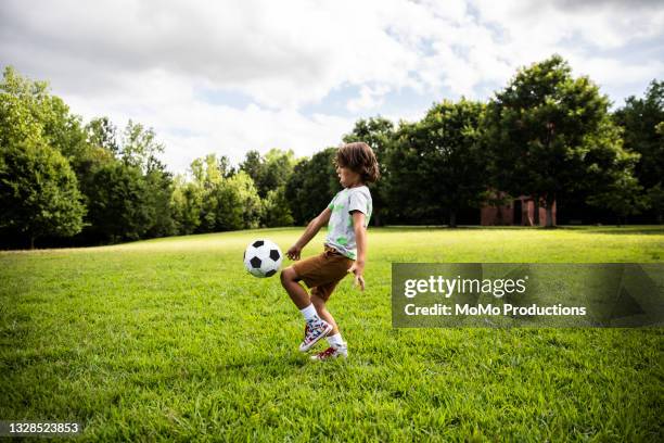young boy playing soccer at park - jugar fotografías e imágenes de stock