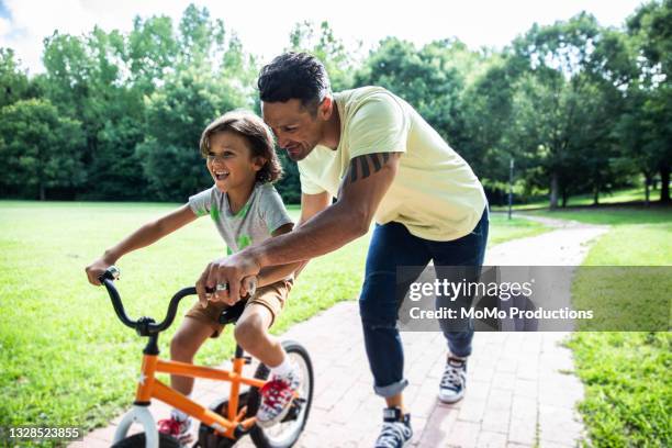 father teaching son to ride a bicycle - buitensport stockfoto's en -beelden