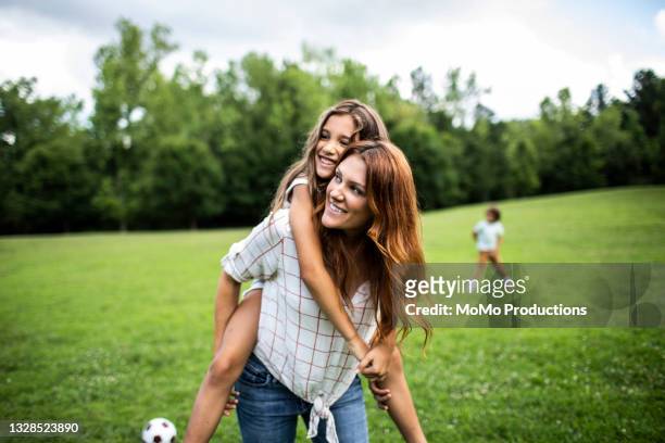 daughter riding on mothers shoulders at park - frauen glücklich natur stock-fotos und bilder