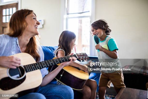 mother and daughter playing guitar while son sings into a hairbrush - daughter band foto e immagini stock
