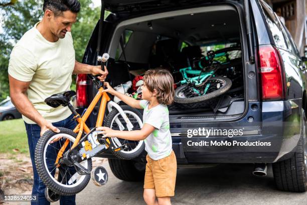 father and son loading bicycles into car - caricare attività foto e immagini stock