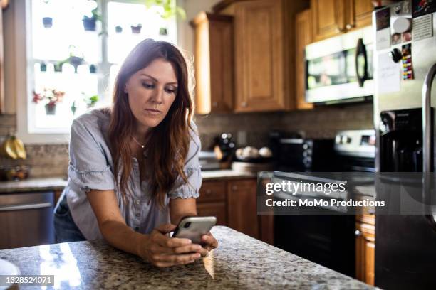 woman using mobile device in kitchen at home - woman texting fotografías e imágenes de stock