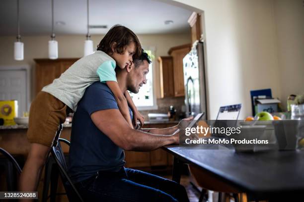 father using laptop while son looks over his shoulder - kitchen internet photos et images de collection