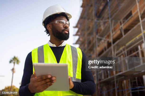 young black male project manage con giubbotto di sicurezza e casco - construction workers foto e immagini stock