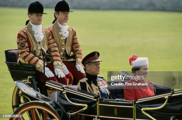 British Royals Prince Philip, Duke of Edinburgh , and Queen Elizabeth II, wearing a red coat with a red-and-white hat by Ian Thomas, riding in a...