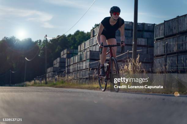 back light photo of a young woman cyclist, pedaling her road bike fast with force, on a paved road in the middle of a wheat field. 3/3 photo motion - fast motion stock pictures, royalty-free photos & images