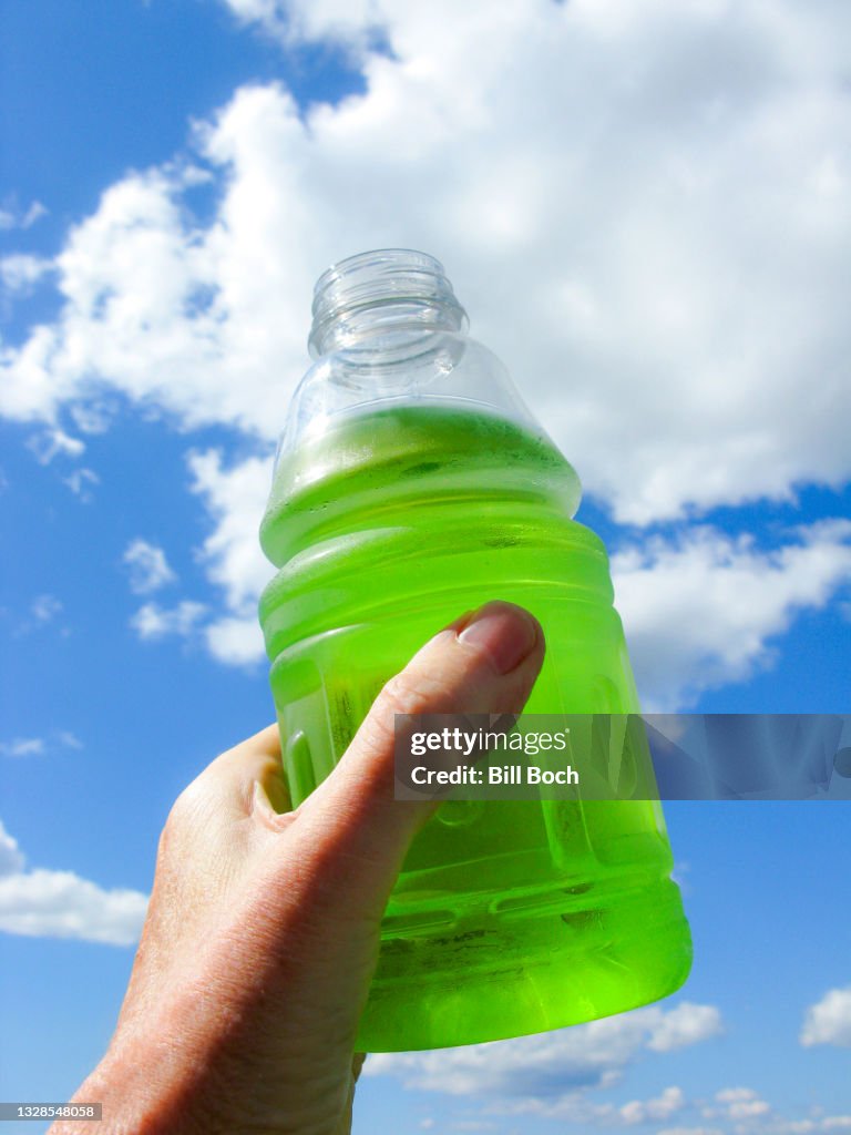 Sport drink in a hand raised to the sky with a cloudscape, in a salute to sports - part of a series