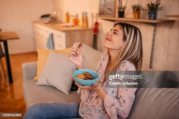 schöne frau, die zu hause kekse isst - biscuit stock-fotos und bilder