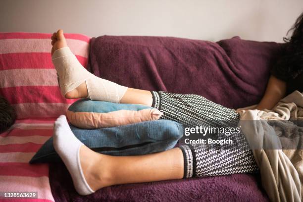 injured hispanic woman elevating bandaged sprained angle on the sofa - personal injury stockfoto's en -beelden