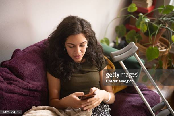 vista de alto ángulo de la mujer millennial lesionada enviando mensajes de texto en casa - crutches fotografías e imágenes de stock