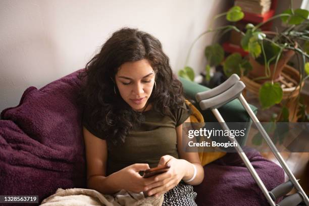 high angle view of injured millennial woman texting at home - crutch stock pictures, royalty-free photos & images