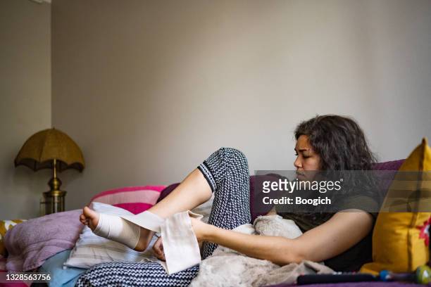injured hispanic woman wrapping sprained angle with bandage at home - compression garment stock pictures, royalty-free photos & images