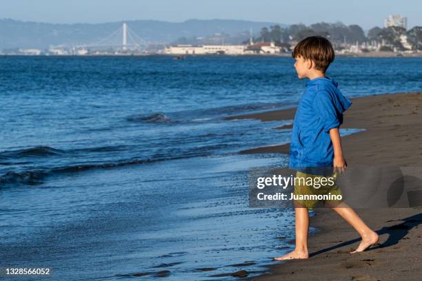 kleiner junge, der am strand spazieren geht - boy barefoot rear view stock-fotos und bilder