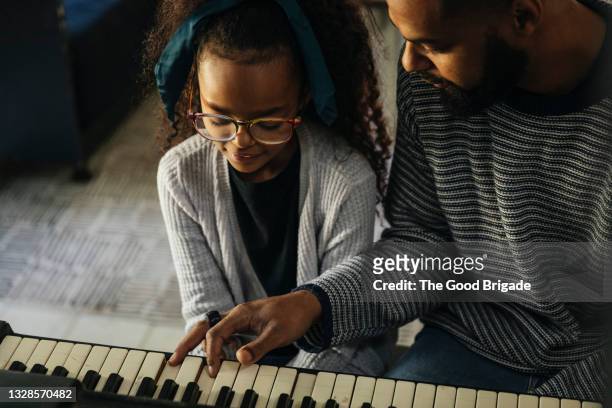 close up of father teaching daughter to play piano at home - playing piano stock pictures, royalty-free photos & images