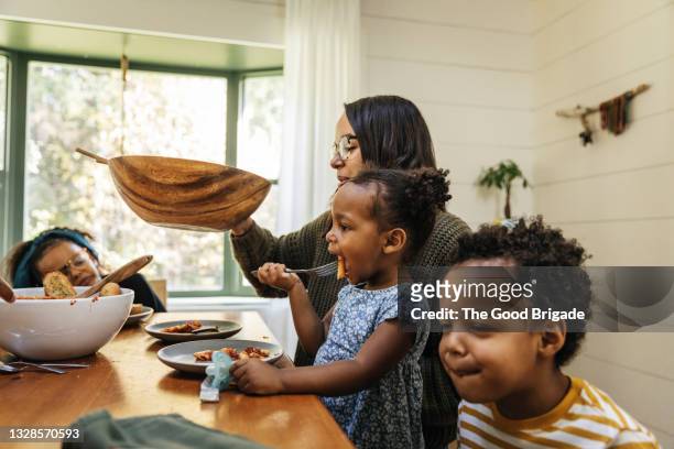 mother passing salad bowl during family meal - familie eten stockfoto's en -beelden
