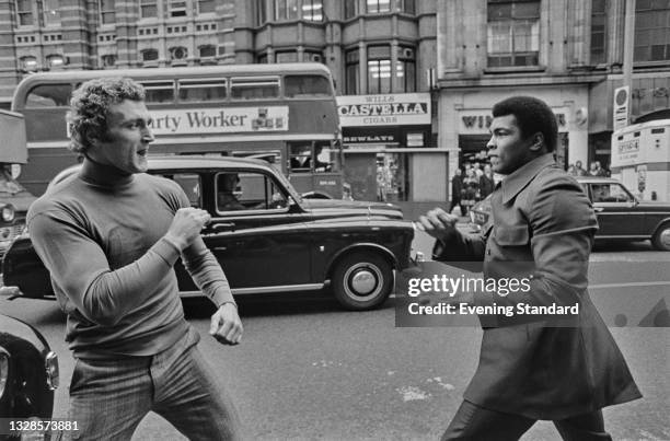 American boxer Muhammad Ali spars with British boxer Joe Bugner outside the Dominion Theatre on Tottenham Court Road in London, UK, 3rd December 1974.