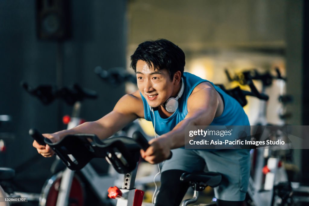 Jeune homme asiatique à vélo stationnaire à la salle de gym. Concept de santé et de remise en forme.