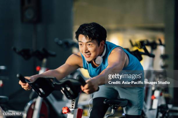 asian young man riding stationary bike at gym. health and fitness concept. - spin class stock pictures, royalty-free photos & images