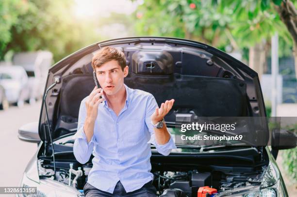 man using the phone to call an insurance company because the car has been damaged by the engine system. - car breakdown stock pictures, royalty-free photos & images