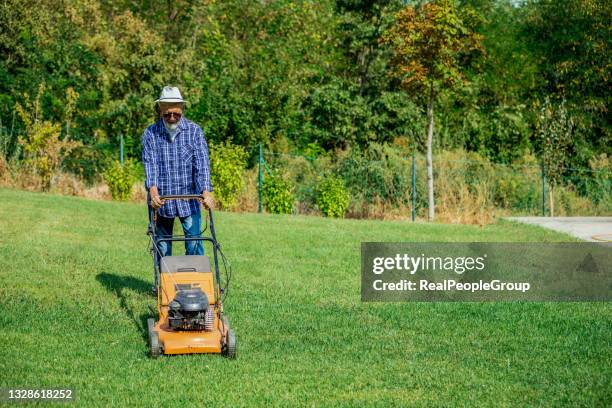 mature man in a good mood mows the grass with  lawn mower in the garden. - handgrasmaaier stockfoto's en -beelden