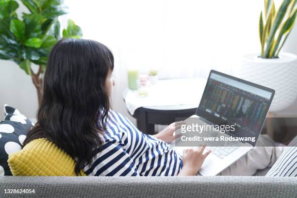 young woman learning online stock trading on laptop while sitting on sofa at home - fundo mútuo de investimento - fotografias e filmes do acervo