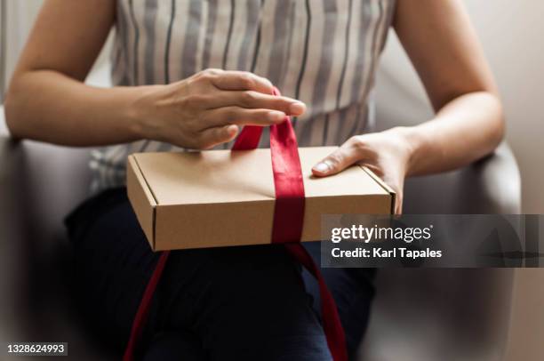 a southeast asian woman is unpacking a small carton box delivery at home - receiving present stock pictures, royalty-free photos & images