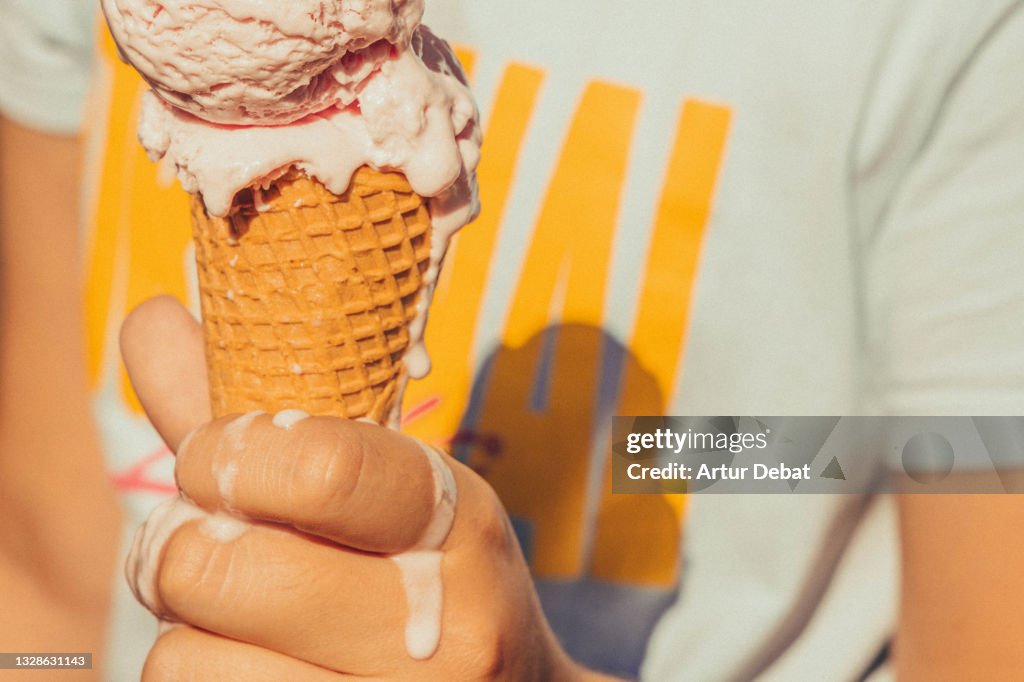Kid holding ice cream cone melting in hot summer.