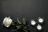 Rose with black ribbon and candles on dark background, flat lay. Space for text
