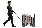 Full length profile shot of a bellboy walking and pushing a trolley cart with suitcases