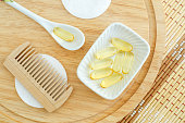Small white bowl with cosmetic oil (face serum, cod fish oil) capsules, cotton pads and wooden hair brush. Natural spa, skin care and beauty treatment recipe. Top view, copy space.