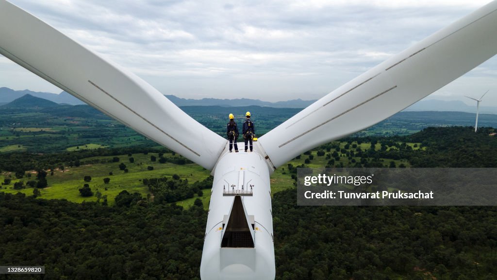 Two Electric engineer wearing Personal protective equipment working  on top of wind turbine farm.