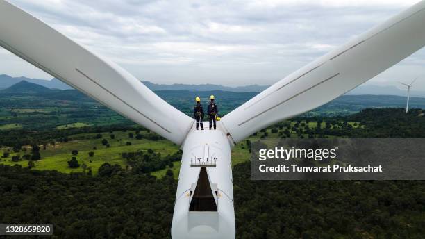 two electric engineer wearing personal protective equipment working  on top of wind turbine farm. - windenergie stockfoto's en -beelden