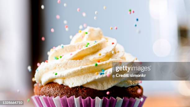 sprinkling hundreds and thousands on cupcake - sprinkling imagens e fotografias de stock