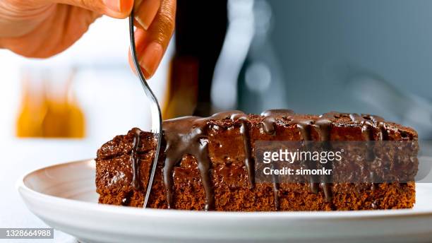 femme coupant une tranche de gâteau au chocolat avec une fourchette - filet de caramel photos et images de collection