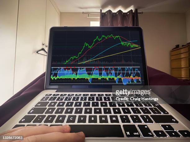 male trading stocks and cryptocurrency from bed on laptop to earn extra money. - earn money stock-fotos und bilder
